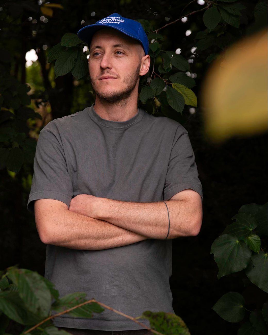 Mat in a blue cap, arms folded, among leaves